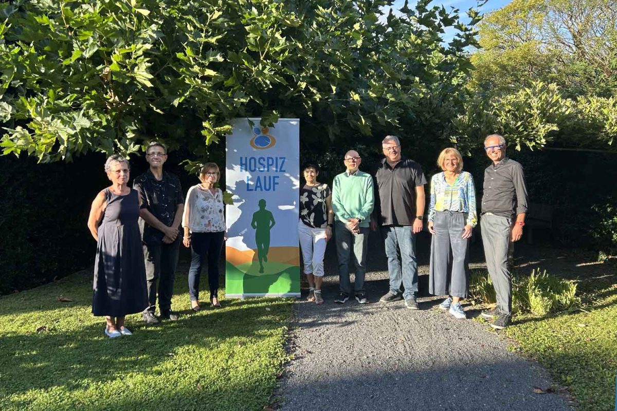 Das Orgateam-Hospizlauf und das Team des Hospiz Trier stehen bei der Spendenübergabe vor dem Hospiz-Roll-Up